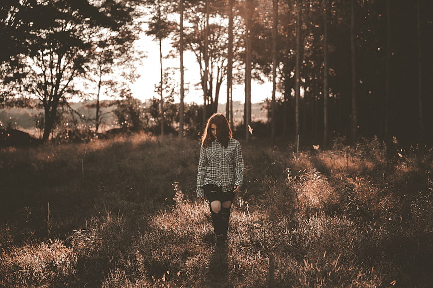 Woman Walking Through Sunlit Forest Path at Sunset