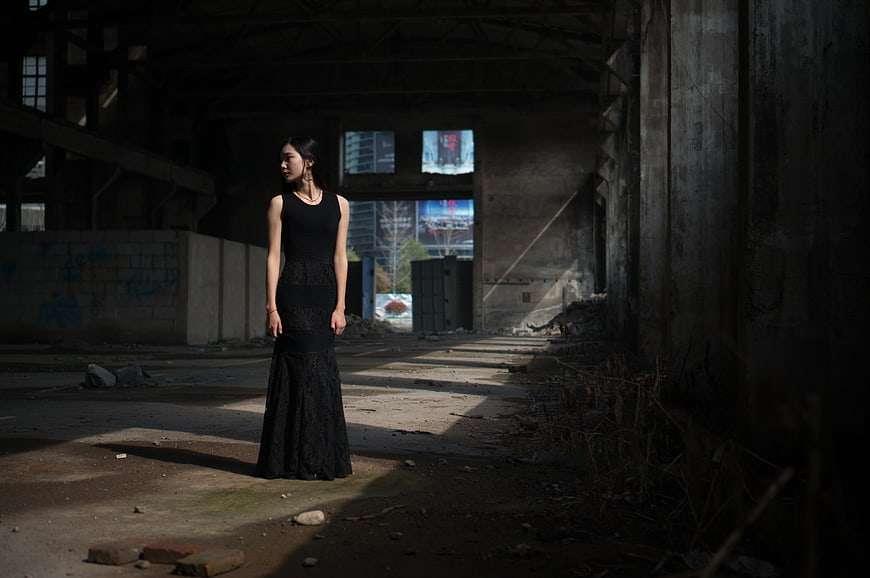 Woman in black dress standing in abandoned industrial ruins