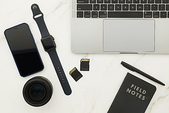 Flat lay of tech gadgets, camera lens, and notebook on marble