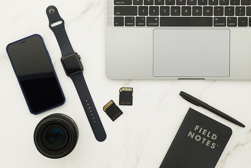 Flat lay of tech gadgets, camera lens, and notebook on marble