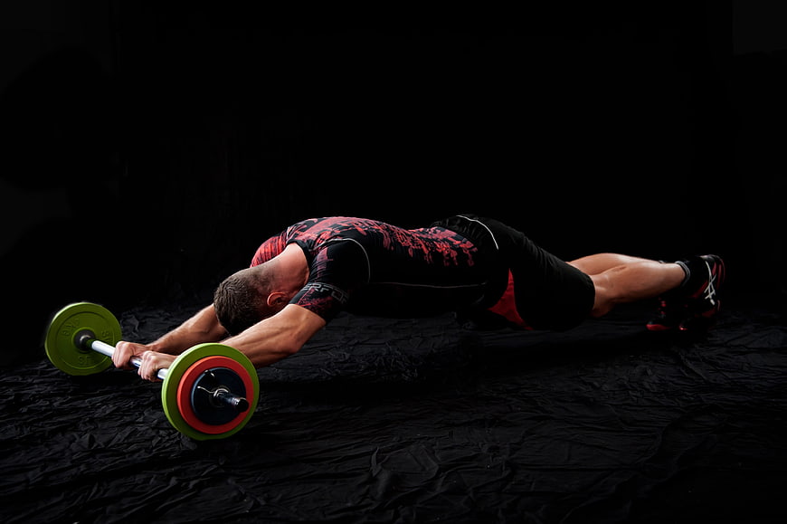 Athletic man performing barbell row exercise in dark gym