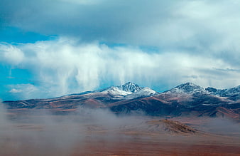 Snow-capped mountains with dramatic clouds and misty foreground