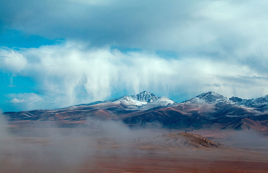 Snow-capped mountains with dramatic clouds and misty foreground