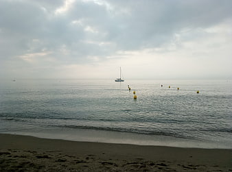 Serene Mediterranean beach with sailboat and yellow buoys