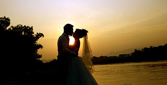Silhouette of Bride and Groom Kissing at Sunset by River