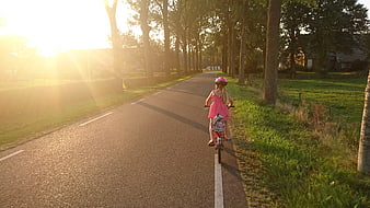 Little Girl Riding Bicycle on Country Road at Sunset