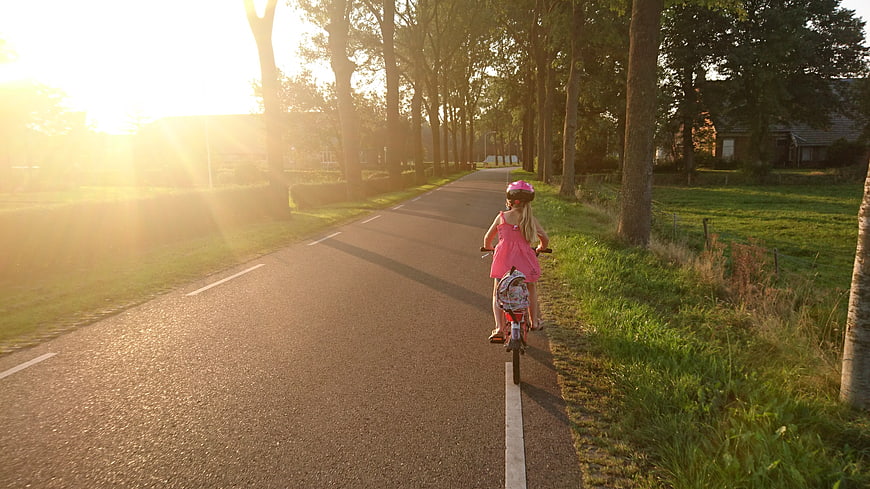 Little Girl Riding Bicycle on Country Road at Sunset