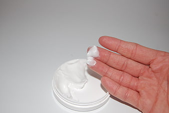 Hand applying white cosmetic cream from open jar on white background