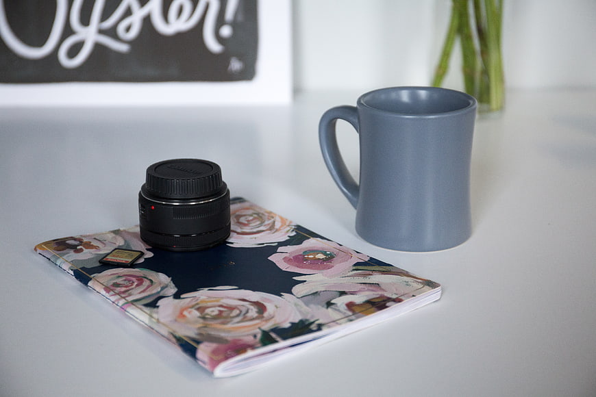 Camera lens on floral notebook with blue coffee mug
