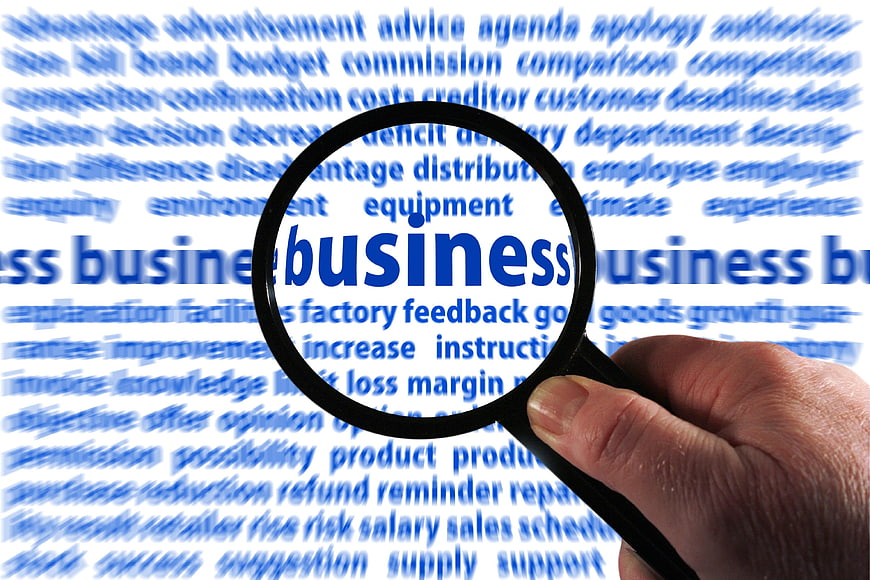 Hand holding magnifying glass over business word cloud