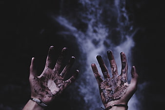 Dirty hands reaching towards smoke in dark background