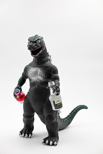 Godzilla toy figure holding two small liquor bottles on white background