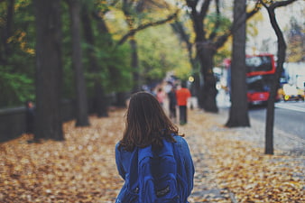 Woman with Blue Backpack Walking on Autumn Sidewalk