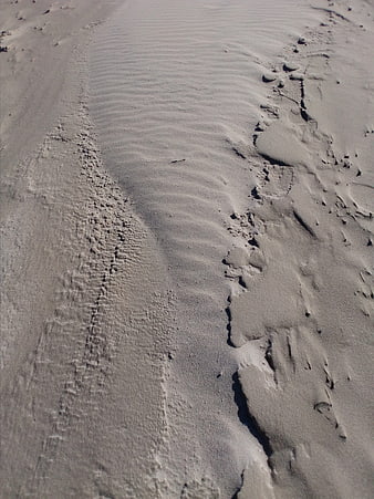 Close-up of textured sand ripples and footprints on a beach