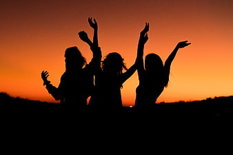 Silhouette of three friends celebrating at sunset