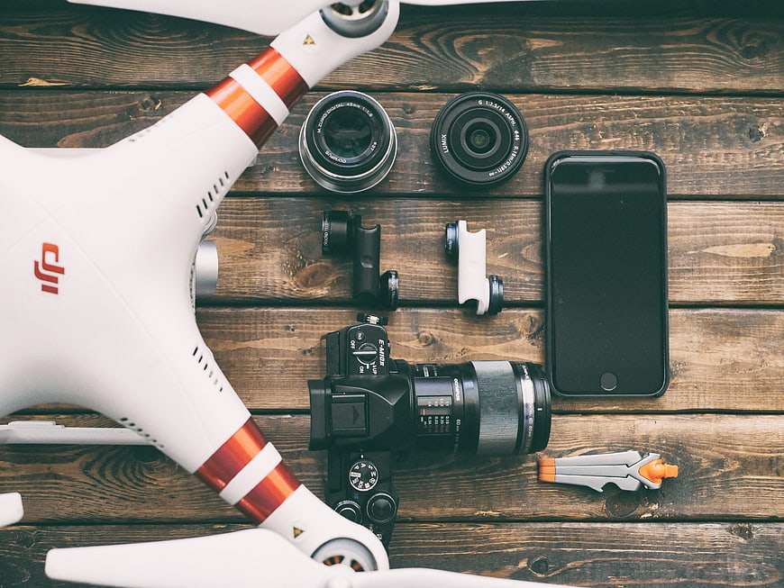 Flat lay of drone, camera, lenses, and smartphone on wooden table