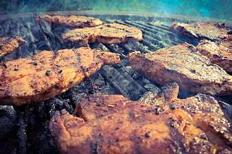 Close-up of seasoned steaks grilling over charcoal with smoke