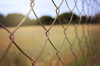Close-up of rusty chain-link fence with blurred field background