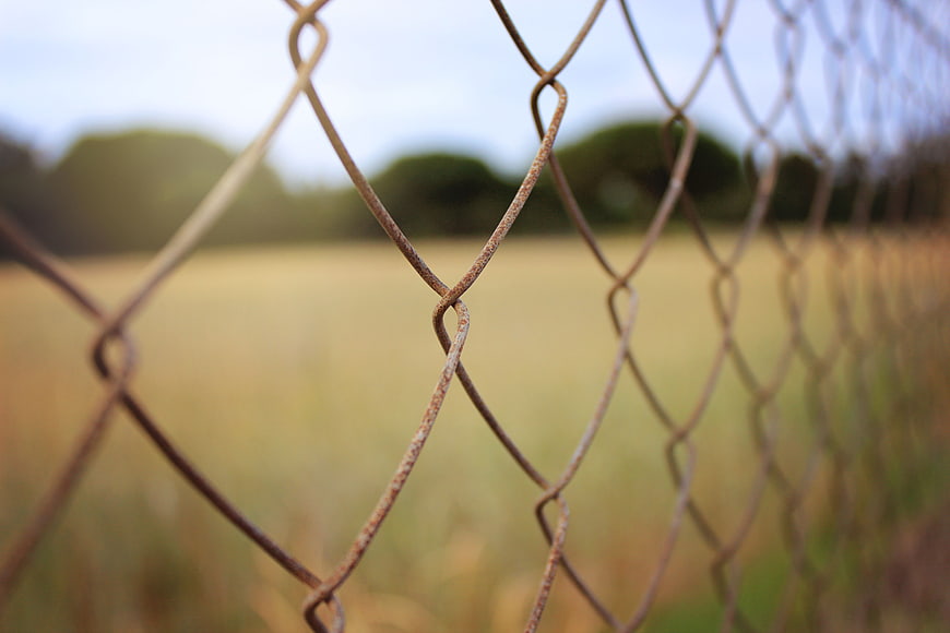 Close-up of rusty chain-link fence with blurred field background