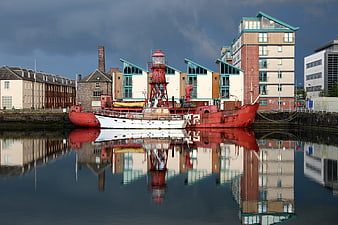 Red and white boat moored in a harbor with building reflections