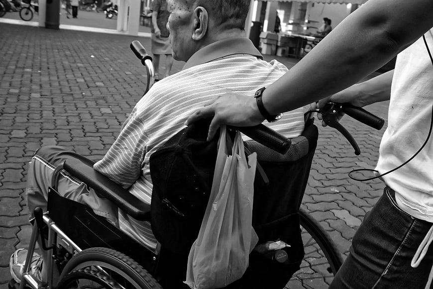 Black and white photo of elderly man in wheelchair being pushed