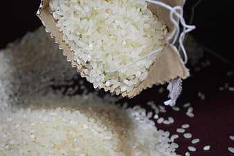 Close-up of white rice grains spilling from a torn paper bag