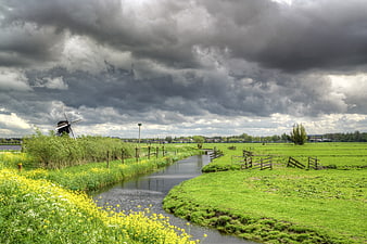 Dutch landscape with windmill and canal under stormy sky