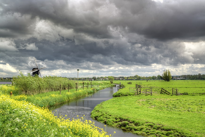 Dutch landscape with windmill and canal under stormy sky
