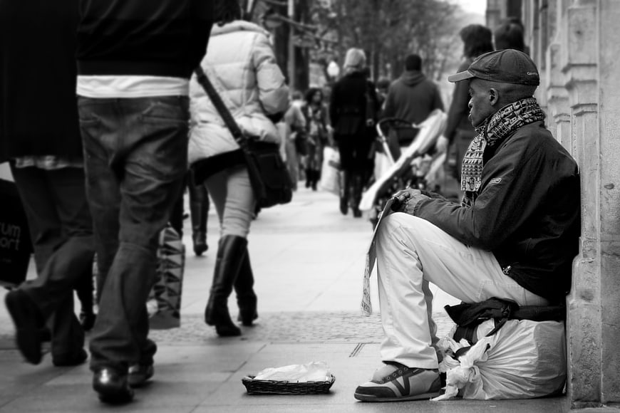 Black and white photo of homeless man sitting on city sidewalk