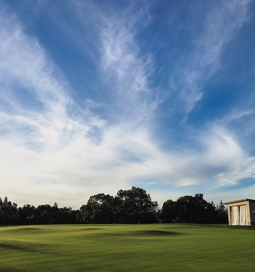 Wide shot of a green golf course with blue sky and clouds