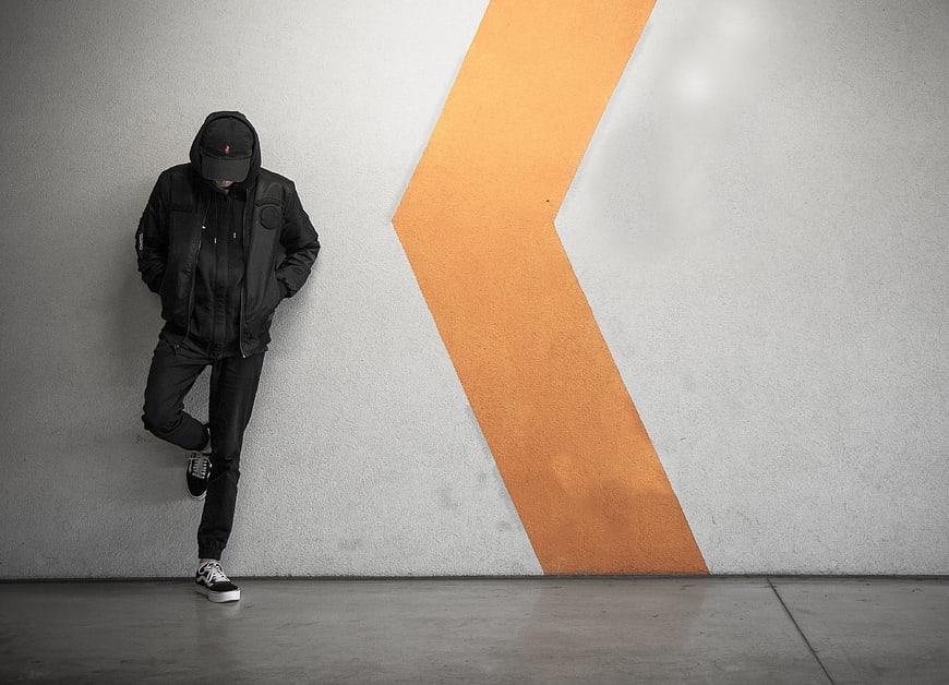 Man in black hoodie leaning against wall with orange arrow