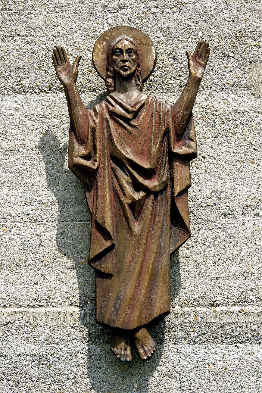 Bronze Statue of Jesus Christ with Raised Hands on Stone Wall