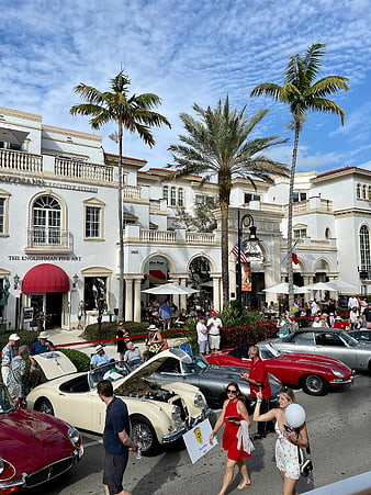 Classic car show on sunny street with palm trees and crowd