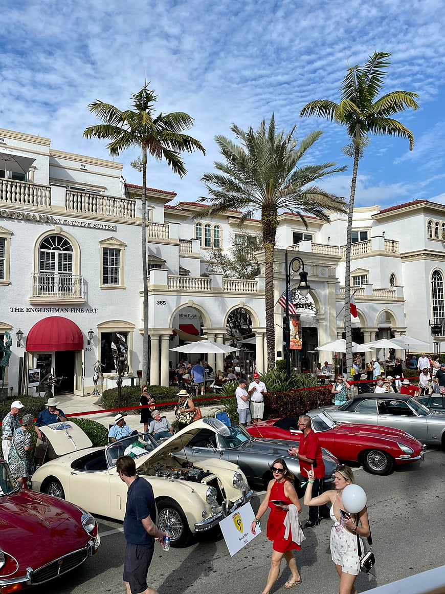 Classic car show on sunny street with palm trees and crowd