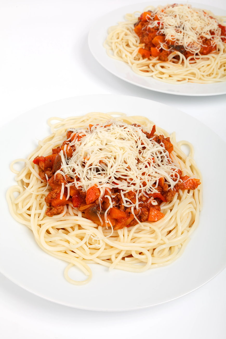 Two plates of spaghetti bolognese with parmesan cheese
