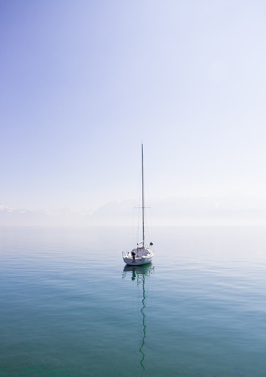 Minimalist Sailboat on Calm Blue Water with Mountain Reflection