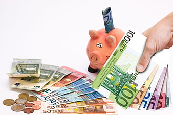Hand inserting Euro banknotes into pink piggy bank with coins