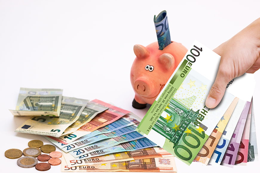 Hand inserting Euro banknotes into pink piggy bank with coins