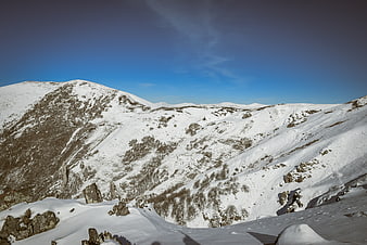 Snow-covered mountain landscape with rocky slopes and blue sky