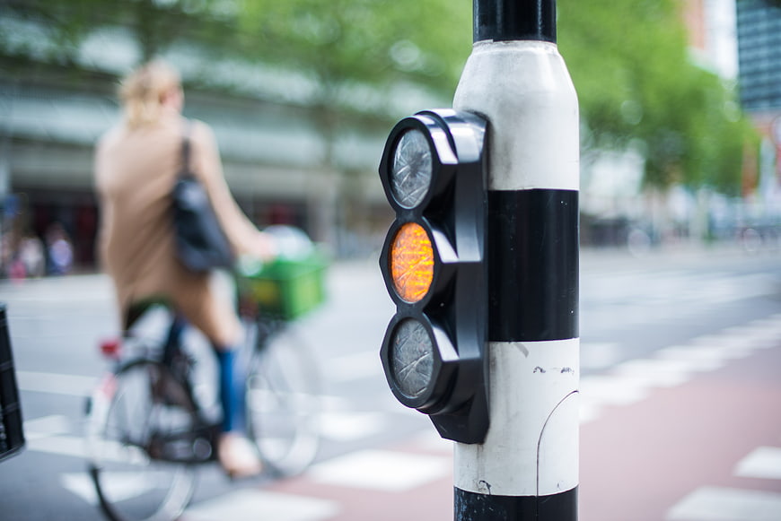 Close-up of amber traffic light with blurred cyclist in background