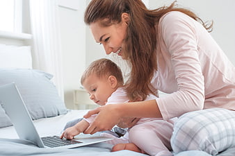 Happy mother and toddler using laptop on bed
