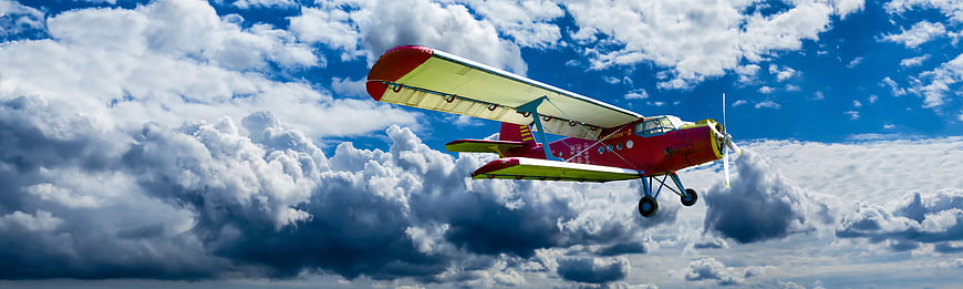 Red and Yellow Biplane Flying Through Blue Sky with Clouds