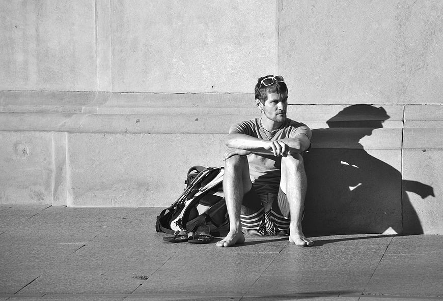 Barefoot man resting against wall in black and white