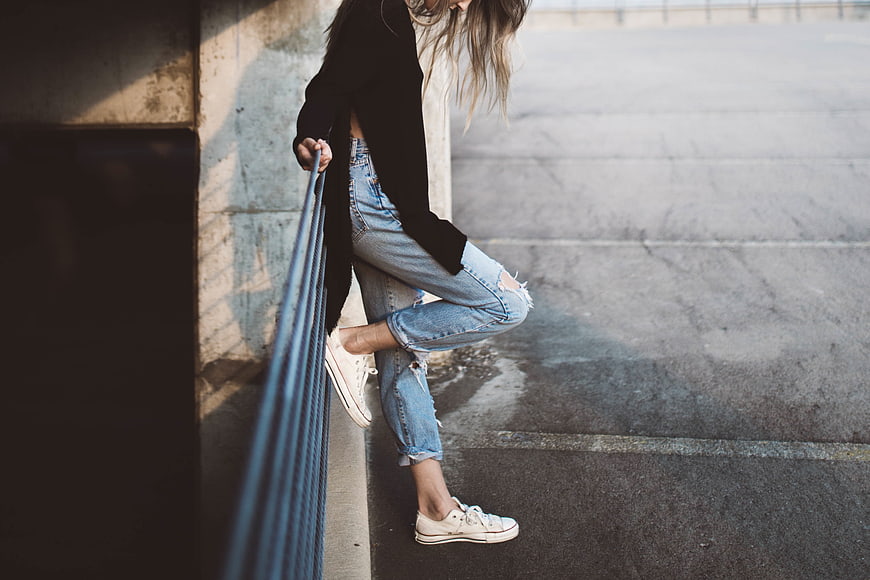 Woman in ripped jeans and sneakers leaning on railing