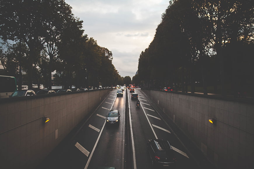 Cars entering a tunnel on a tree-lined avenue at dusk
