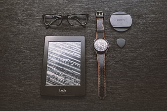 Flat lay of Kindle e-reader, watch, glasses, and camera lens cap