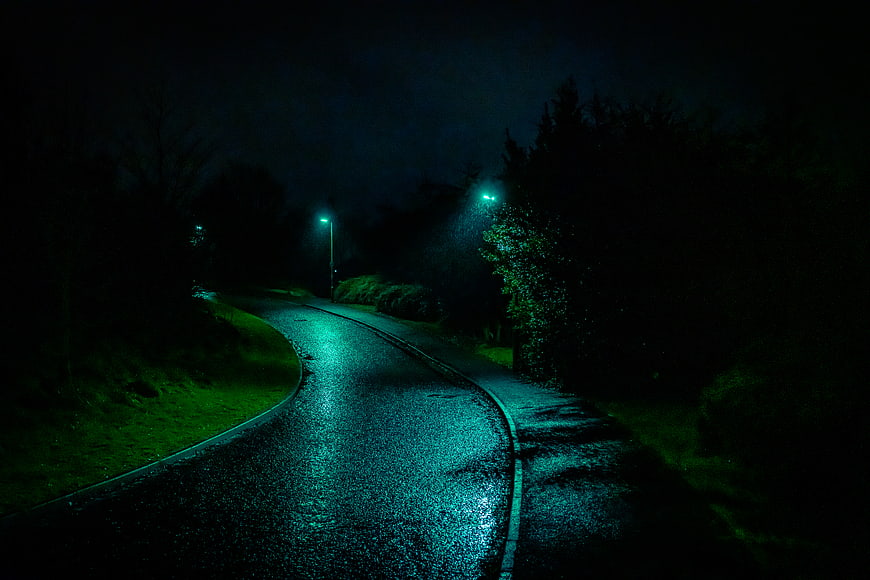 Winding wet road at night with green streetlights