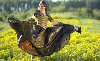 Woman in historical dress twirling in a field of yellow flowers