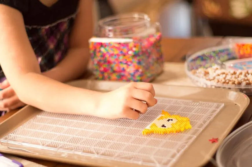 Child making pixel art with colorful beads on tray