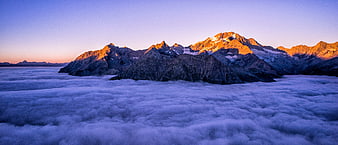 Sunlit mountain peaks rising above a sea of clouds at sunrise